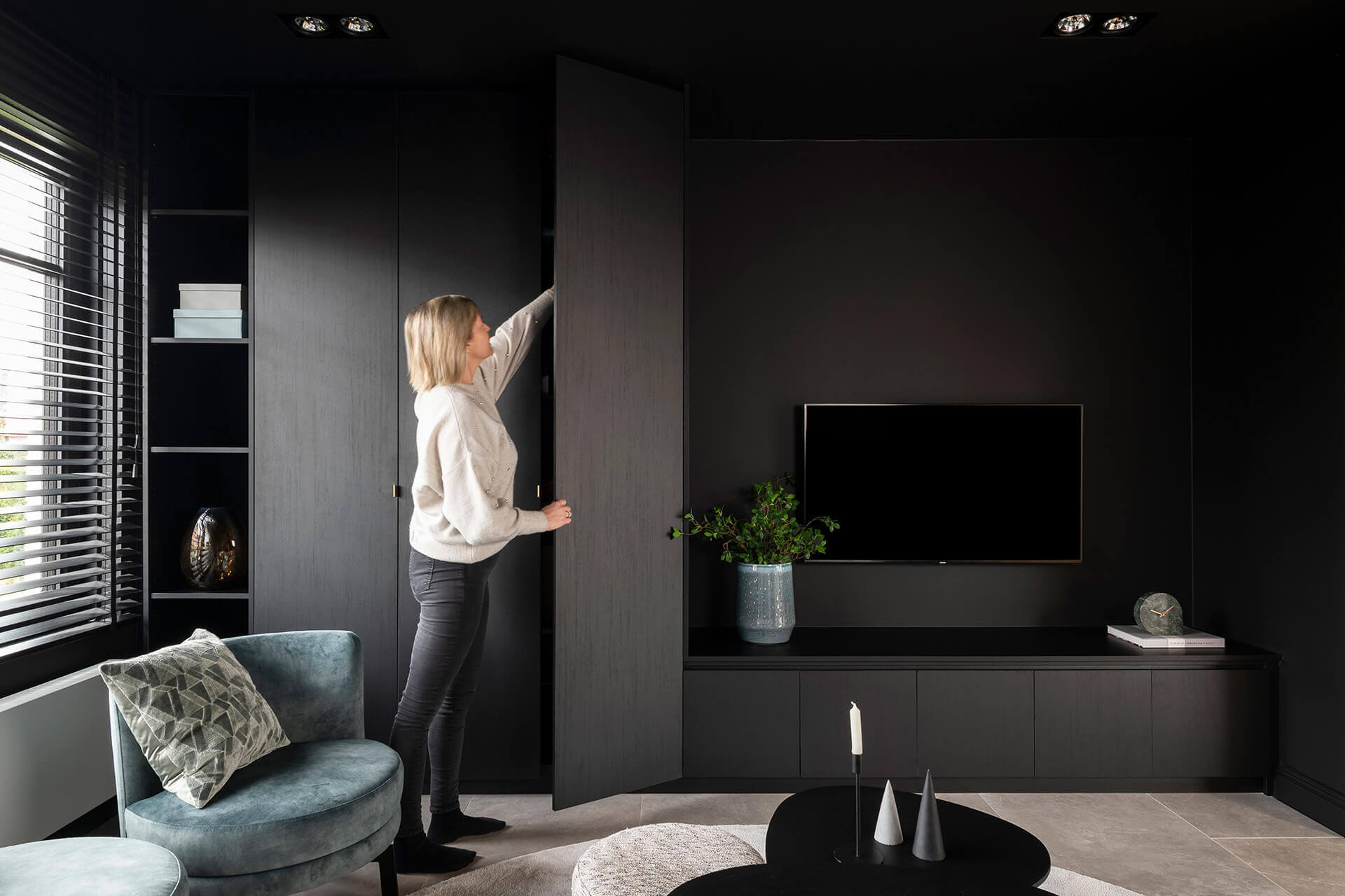 Vrouw staat bij zwarte opbergkasten voor de salon en woonkamer in de kleur Elegant Black, van Maatkasten Online