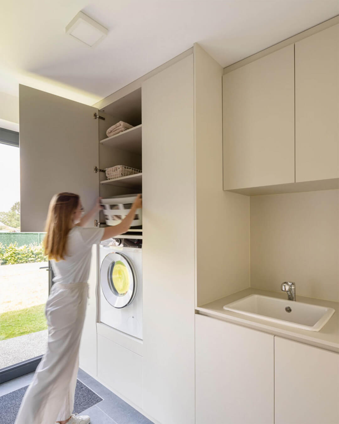 Wall unit of custom high and low cabinets with space for a built-in washing machine in the warm grey color Turtle Grey